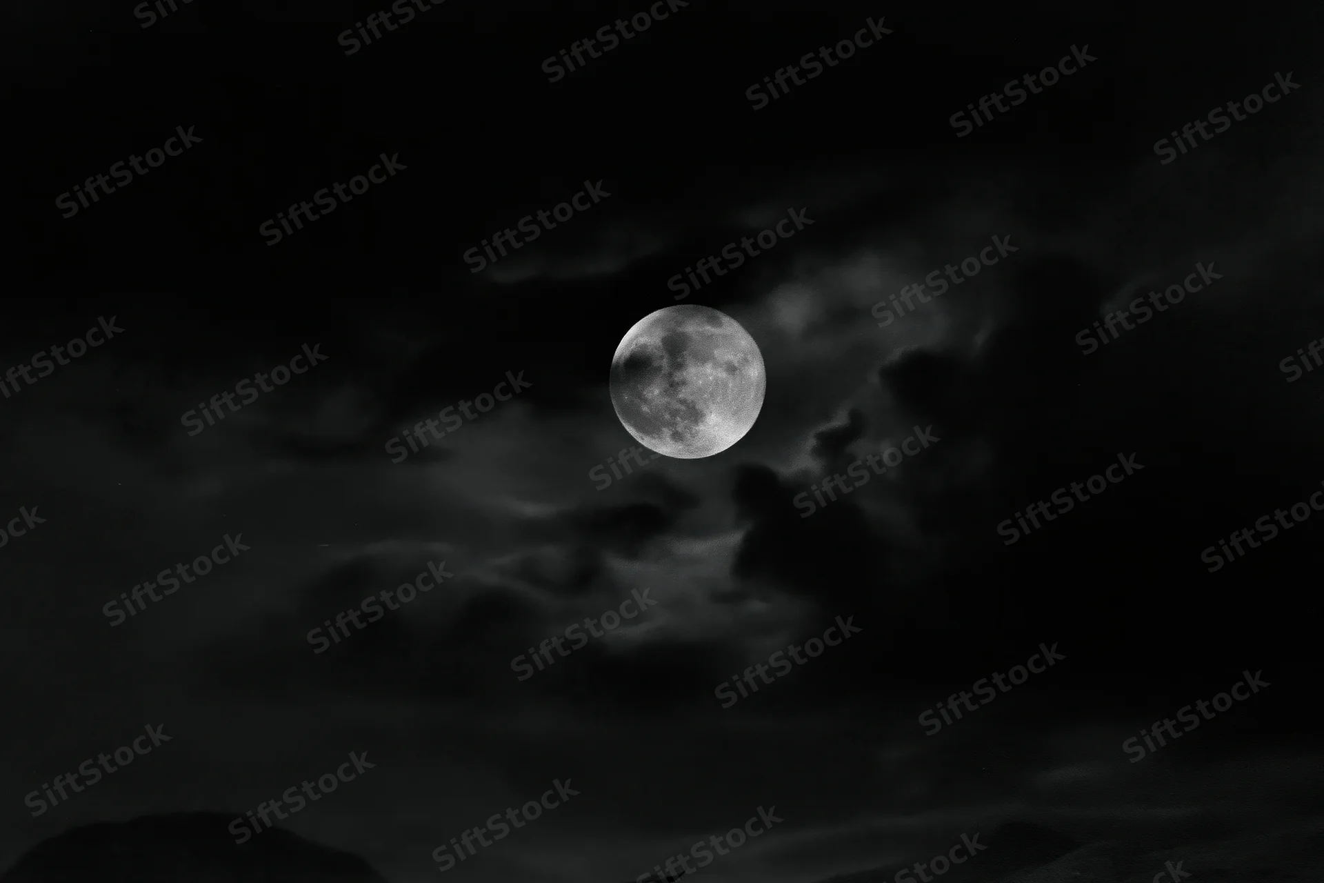 Full moon glowing in dark stormy sky above silhouetted landscape