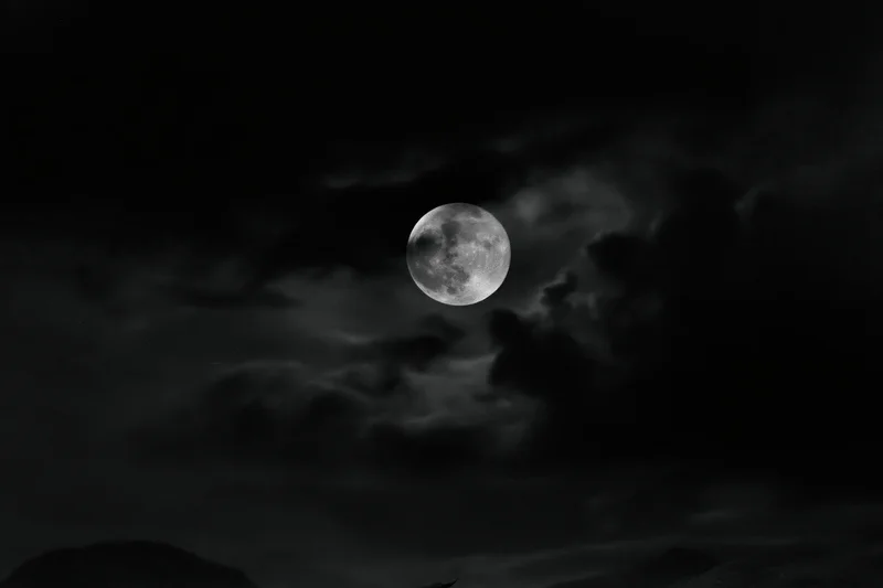 Full moon glowing in dark stormy sky above silhouetted landscape