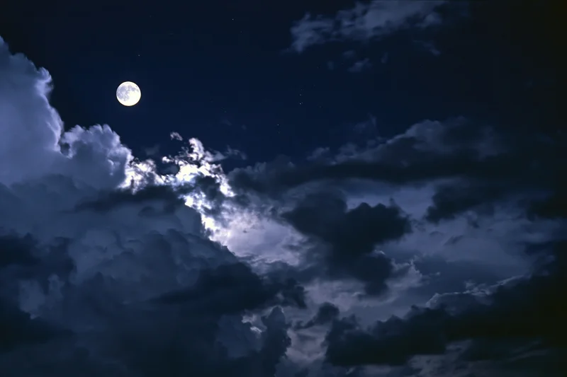 Full moon glowing through dramatic storm clouds in dark night sky
