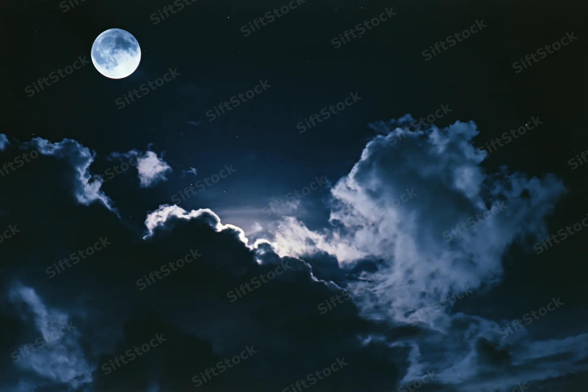 Full moon glowing above dramatic storm clouds in dark night sky