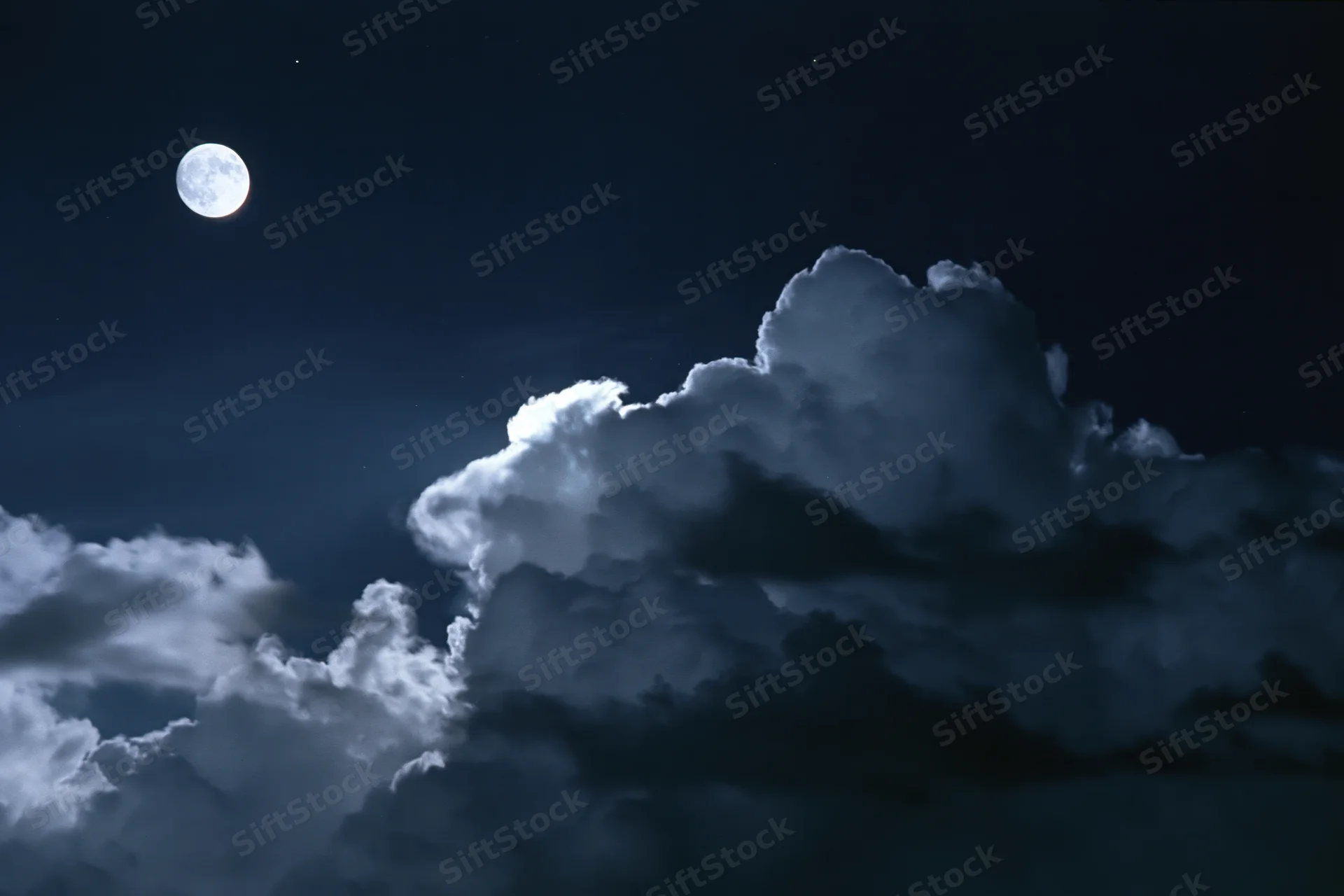 Full moon glowing above dramatic storm clouds in dark night sky