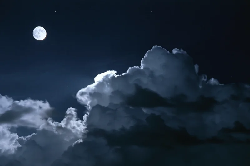 Full moon glowing above dramatic storm clouds in dark night sky