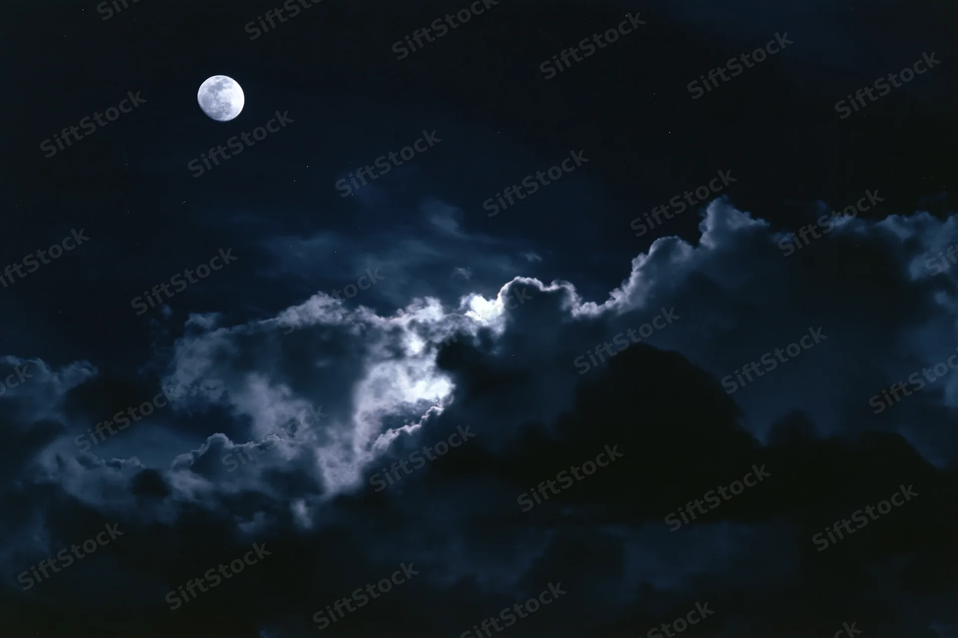 Full moon glowing above dark storm clouds in night sky