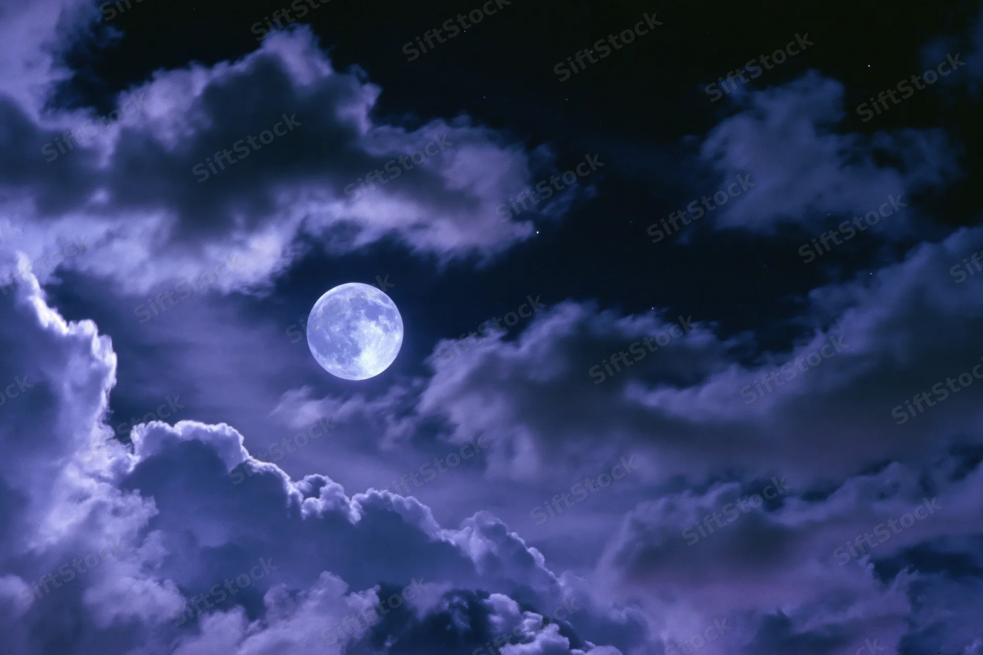 Full moon glowing in a dark sky surrounded by swirling clouds