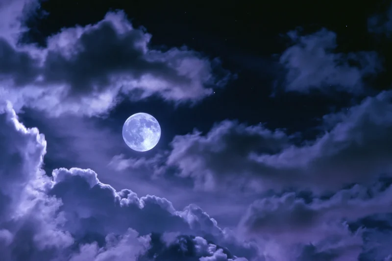 Full moon glowing in a dark sky surrounded by swirling clouds