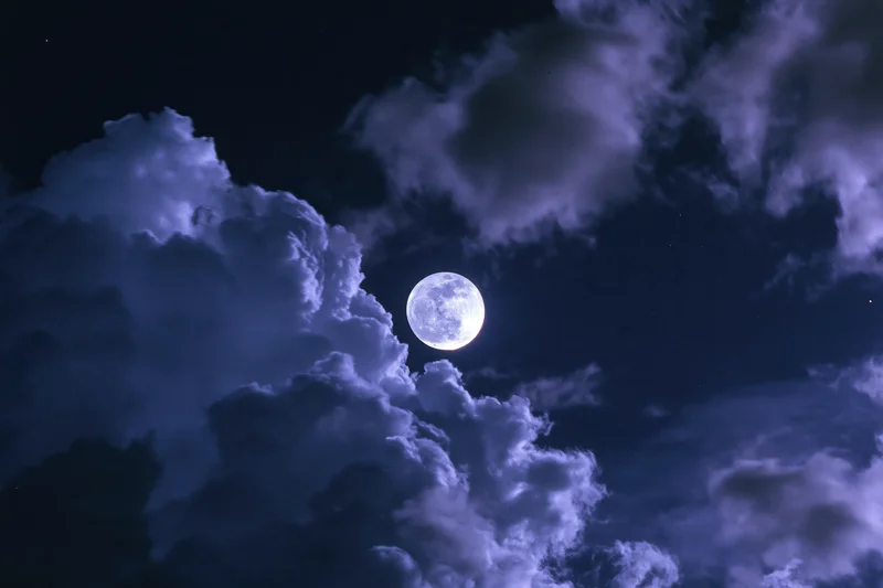 Full moon glowing in dark sky surrounded by dramatic clouds