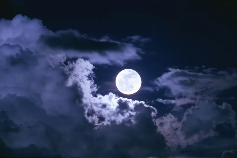 Full moon glowing through dramatic clouds in dark night sky