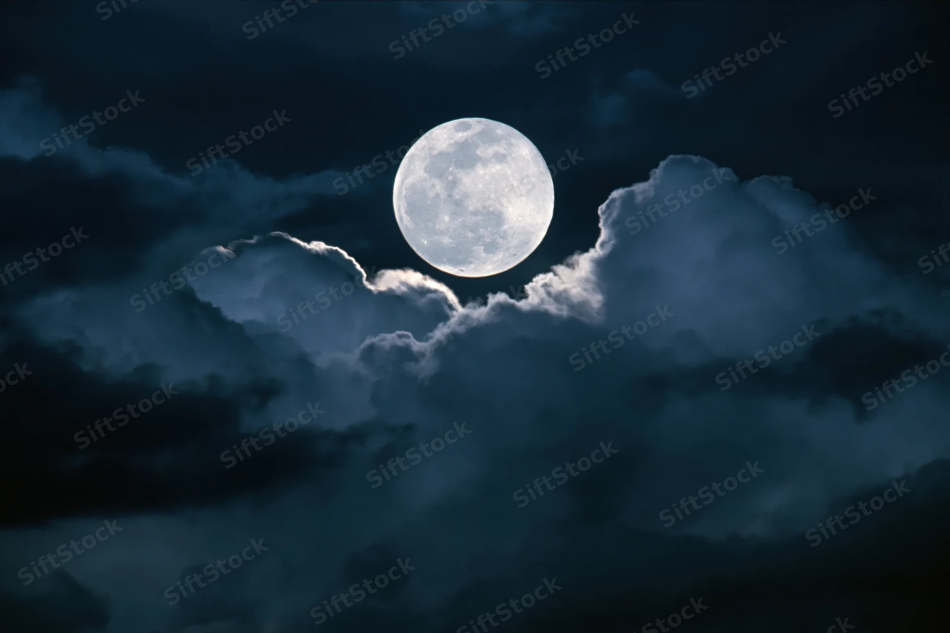 Full moon rising behind dramatic storm clouds at night