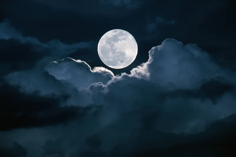 Full moon rising behind dramatic storm clouds at night