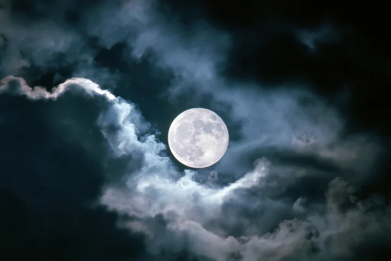 Full moon rising behind dramatic storm clouds at night