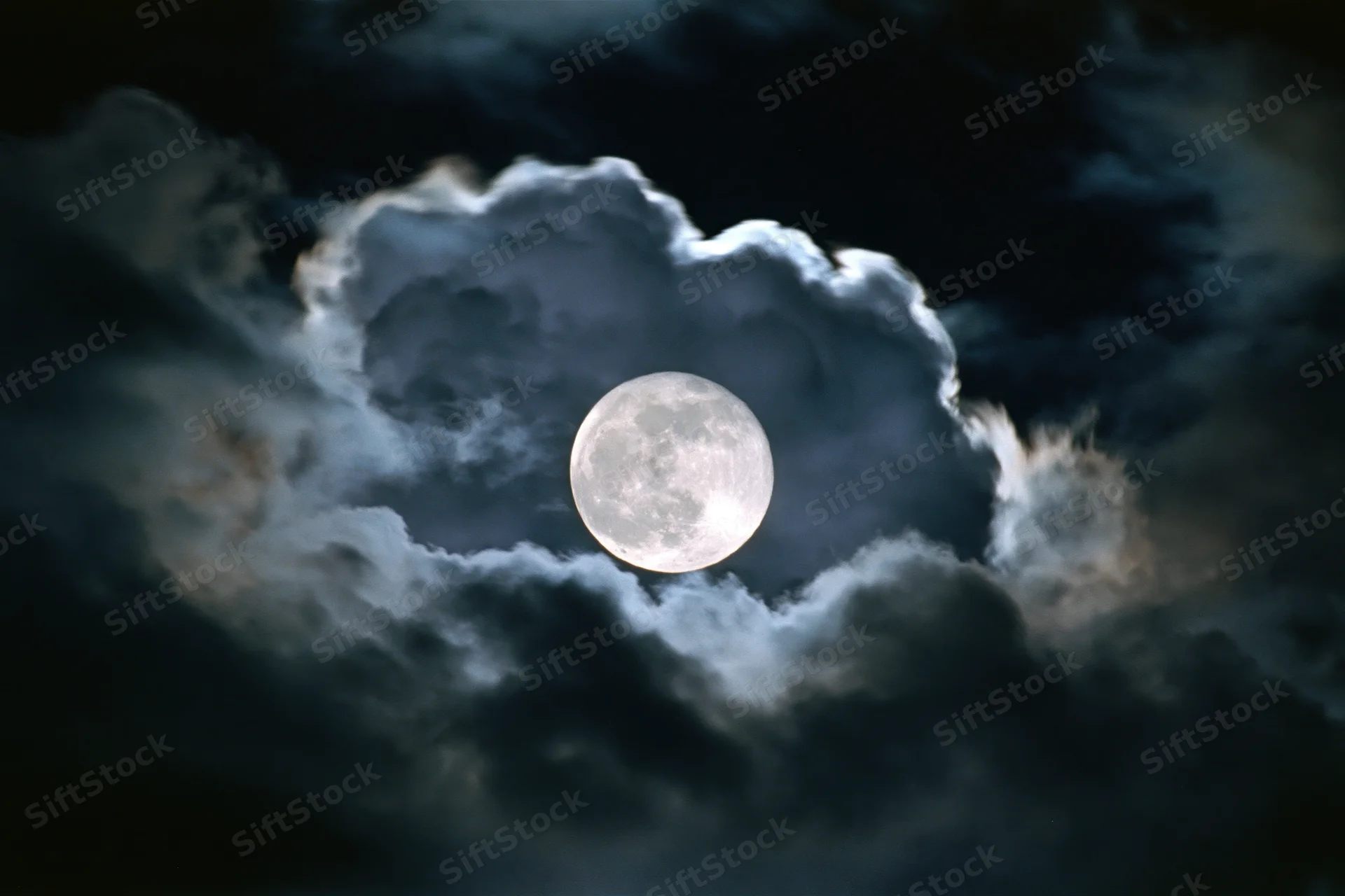 Full moon glowing through dark storm clouds in night sky