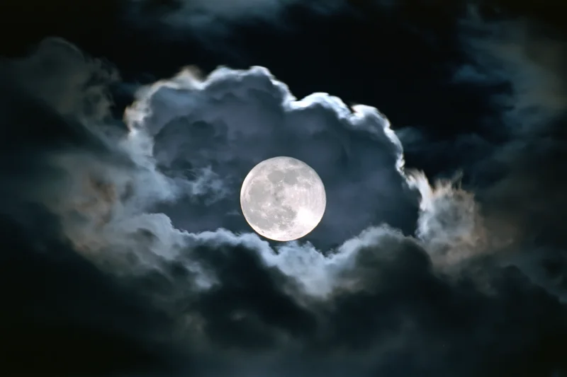 Full moon glowing through dark storm clouds in night sky