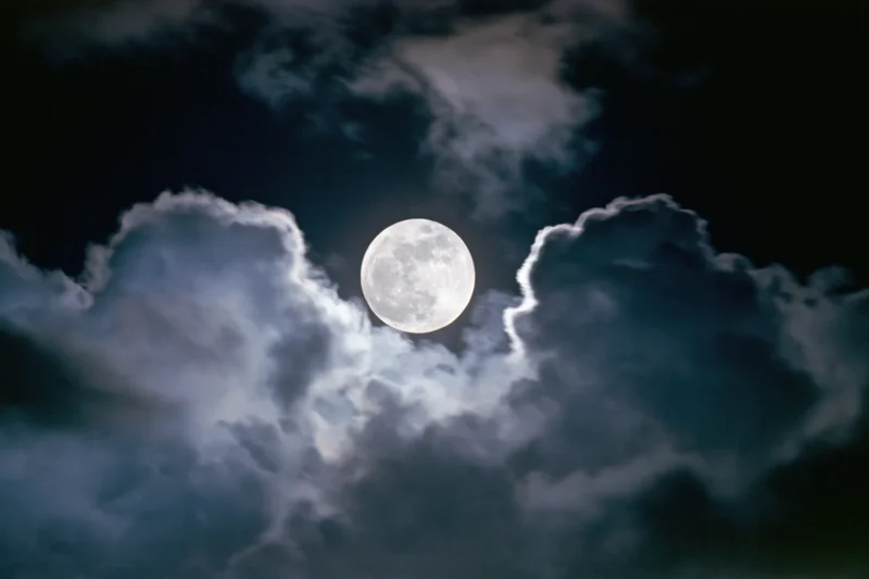 Full moon rising behind dramatic storm clouds at night