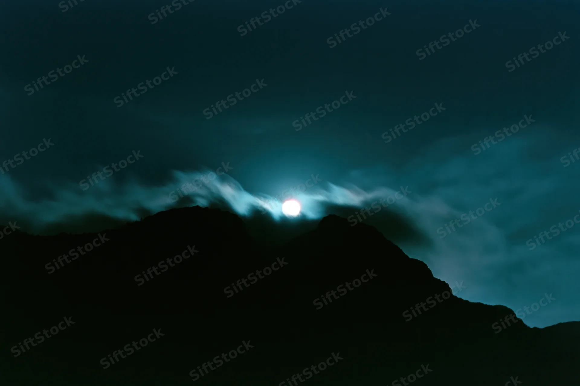 Full moon rising over dark mountain silhouettes in a wide night landscape