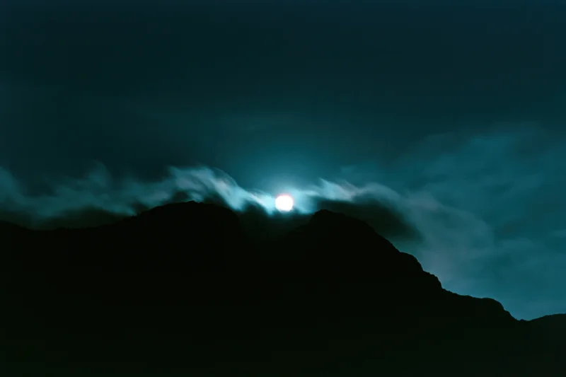 Full moon rising over dark mountain silhouettes in a wide night landscape