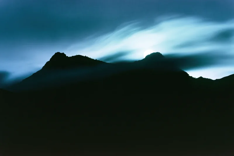 Full moon rising over dark mountain silhouettes in a wide landscape at night