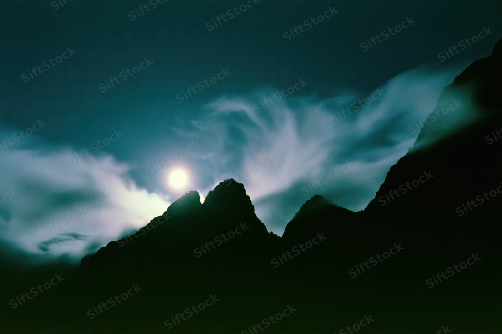 Full moon rising over dark mountain silhouettes in a wide night landscape