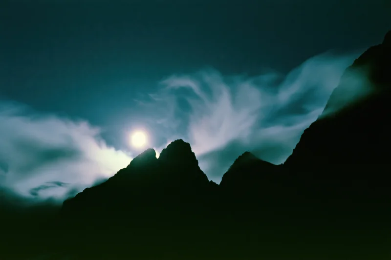 Full moon rising over dark mountain silhouettes in a wide night landscape