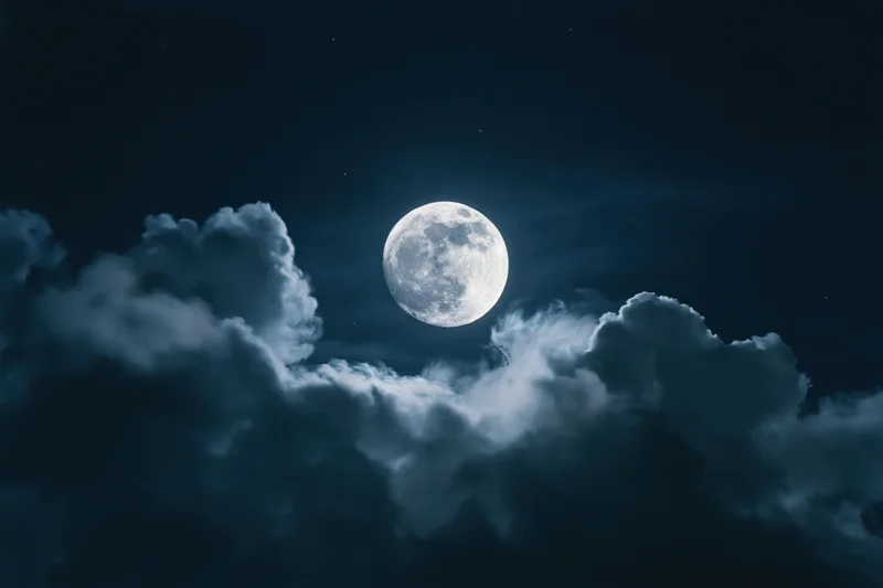 Full moon glowing in dark night sky surrounded by billowing clouds