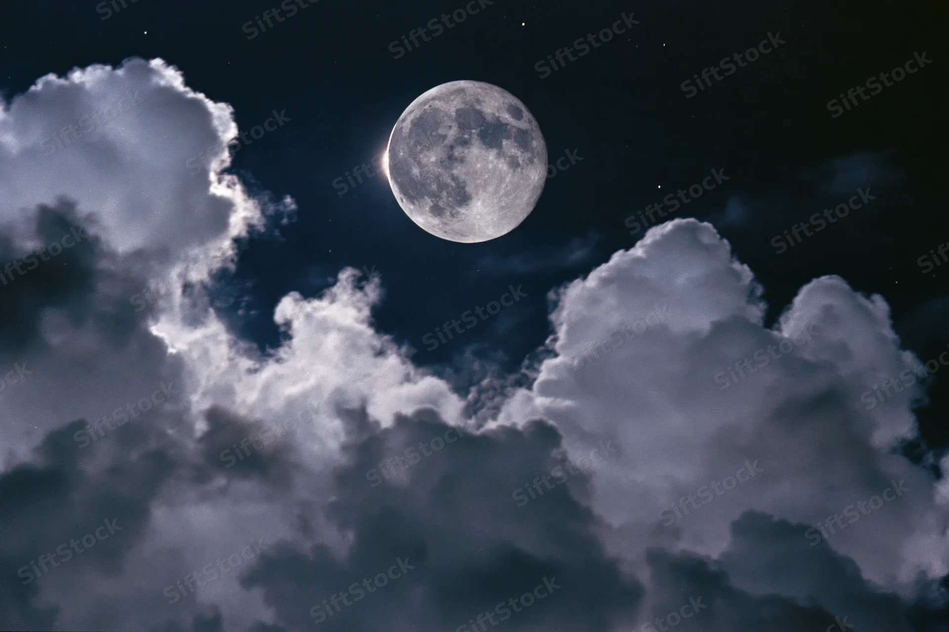 Full moon glowing in dark night sky surrounded by billowing clouds