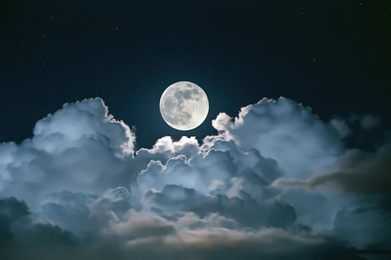 Full moon glowing above billowing clouds in dark night sky