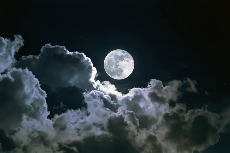 Full moon glowing in dark sky above billowing clouds
