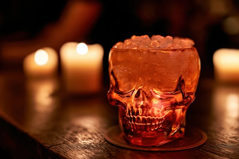 Skull-shaped glass filled with crushed ice on wooden table with candles glowing in background
