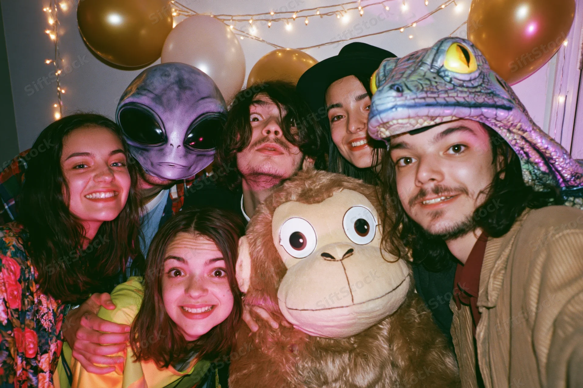 Five young adults posing together at an indoor costume party with masks and balloons