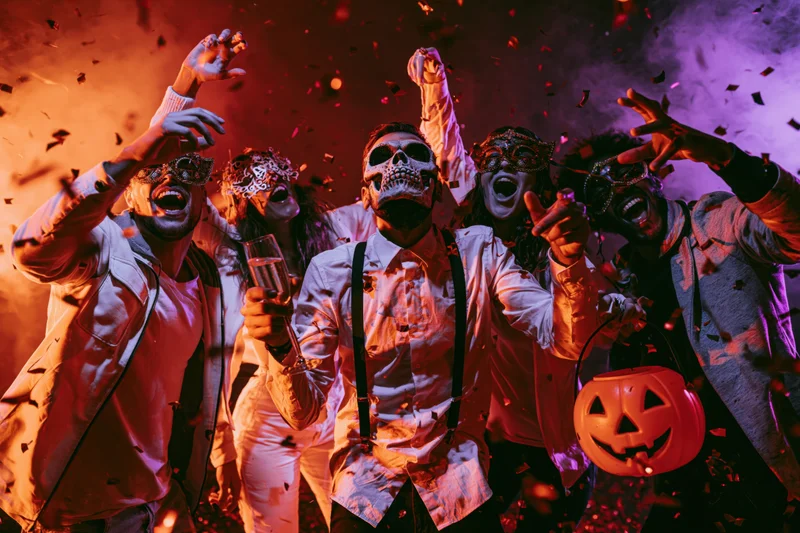 Five young adults in halloween costumes dancing with confetti and smoke at a party