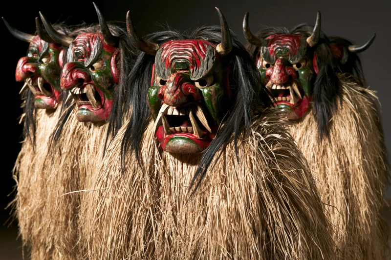 Group of traditional japanese namahage demon figures standing in a row wearing painted wooden masks with horns and straw costumes