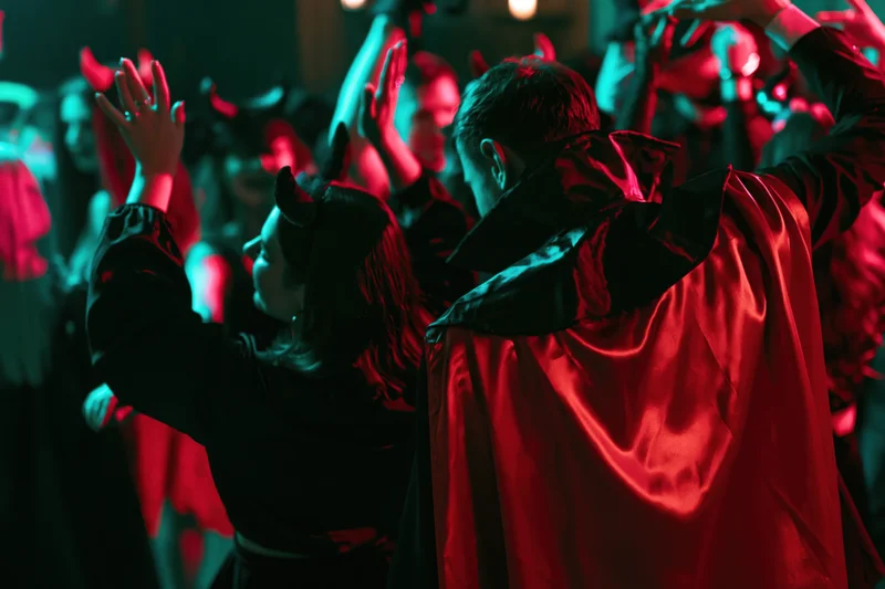 Young adults in devil and vampire costumes dancing at a halloween party under red and green neon lights