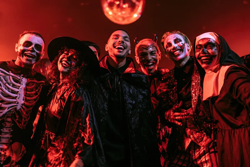 Group of young adults in halloween costumes laughing and dancing at a party under red disco lighting