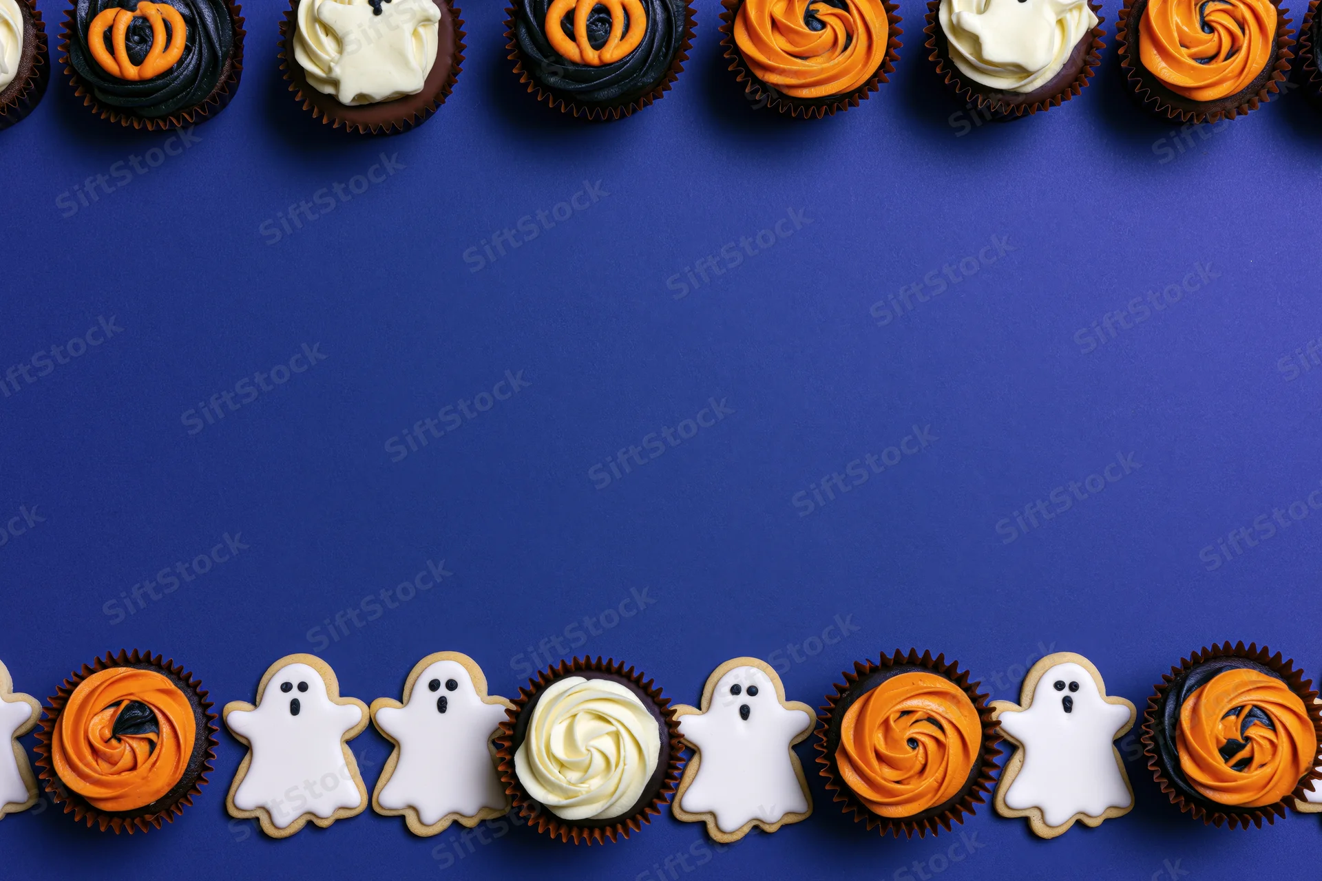 Halloween-themed cupcakes and ghost cookies arranged in rows on blue background with copyspace