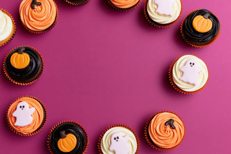 Halloween cupcakes decorated with pumpkins and ghosts arranged in a border on purple background