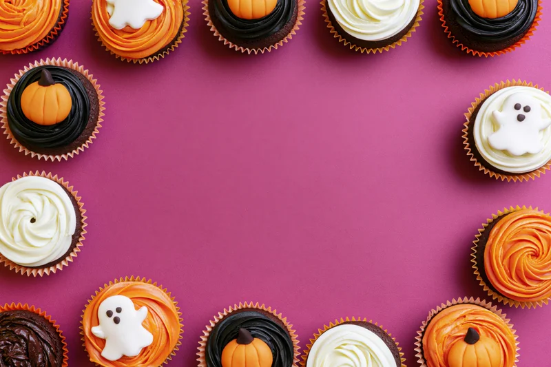 Halloween cupcakes arranged in a border on a purple surface with copyspace in center