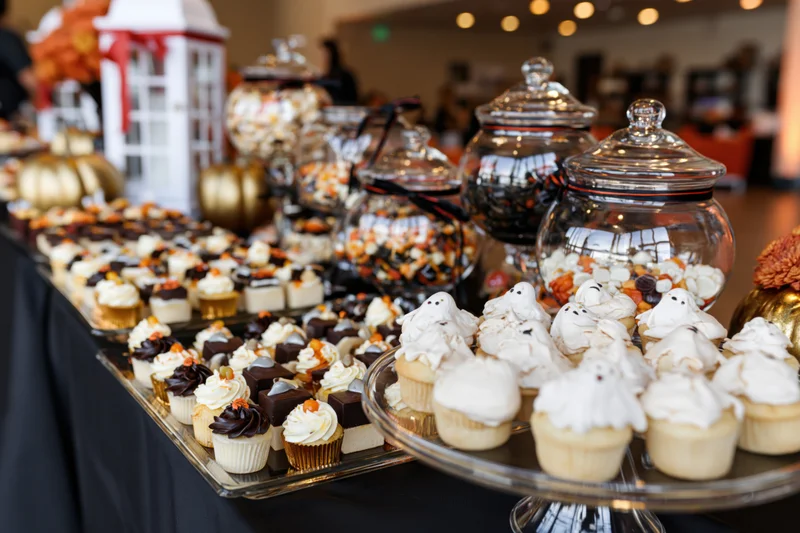 Halloween-themed dessert table with ghost cupcakes and candy jars on a black cloth