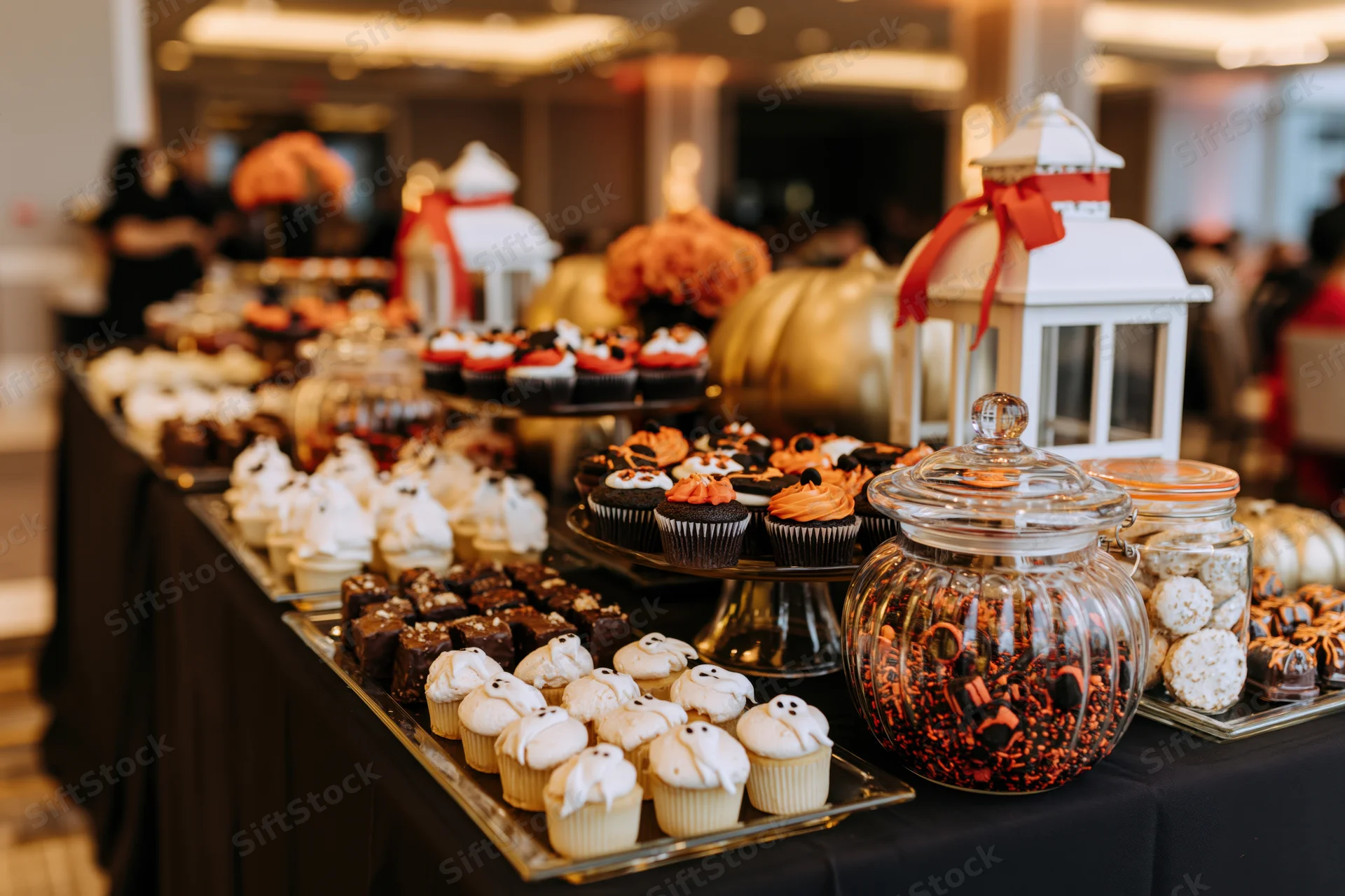 Halloween-themed dessert table with decorated cupcakes and candy jars on a black cloth