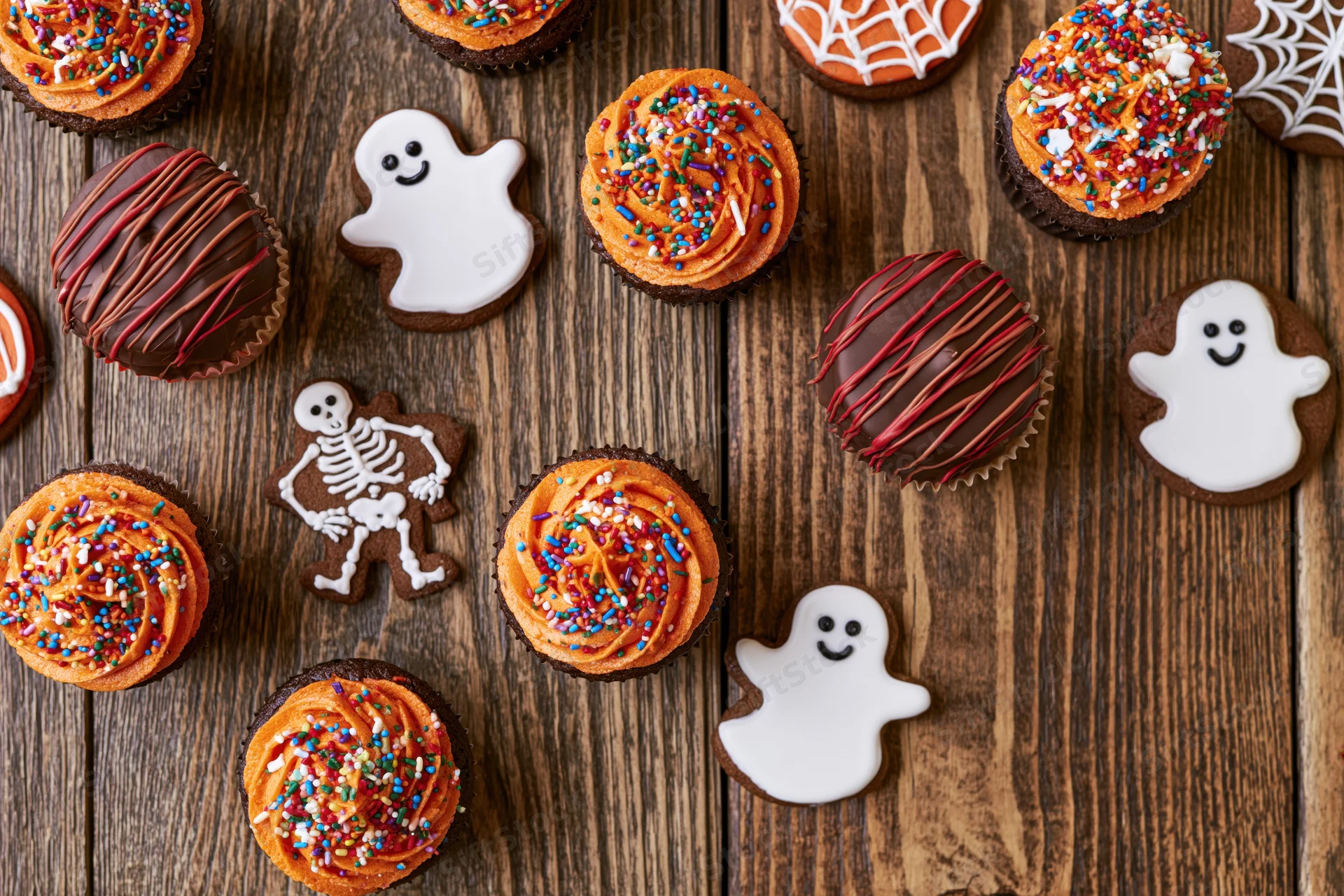 Halloween cupcakes and decorated sugar cookies arranged on a wooden surface