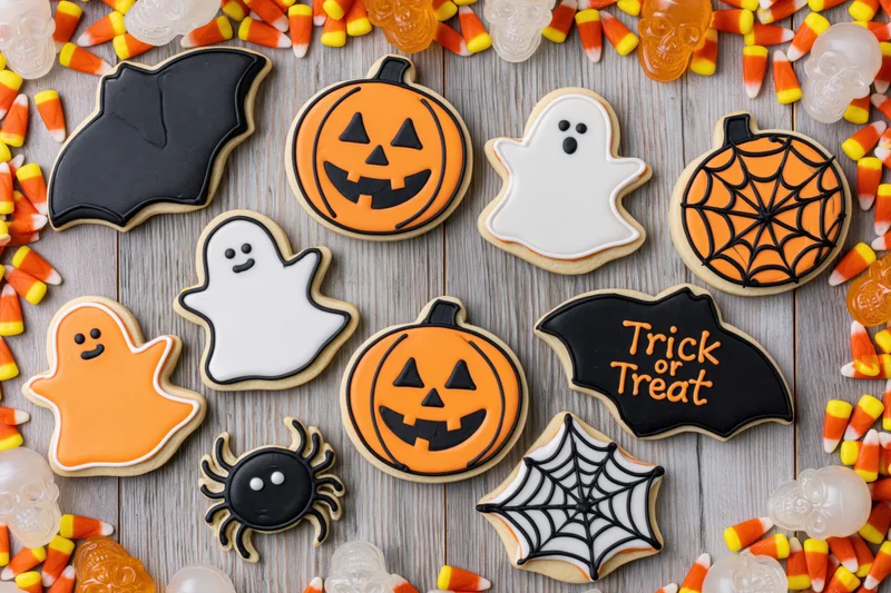 Halloween decorated sugar cookies arranged on wooden surface with candy corn and plastic skulls