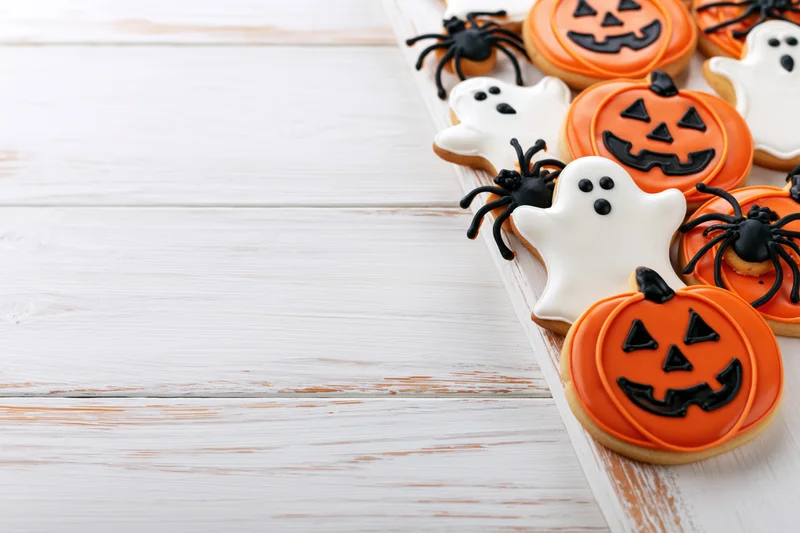 Halloween sugar cookies shaped like jack-o-lanterns, ghosts, and spiders arranged on a white wooden table with copyspace