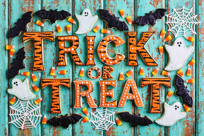 Halloween sugar cookies spelling trick or treat on a turquoise wooden surface with bats, ghosts, and candy corn decorations