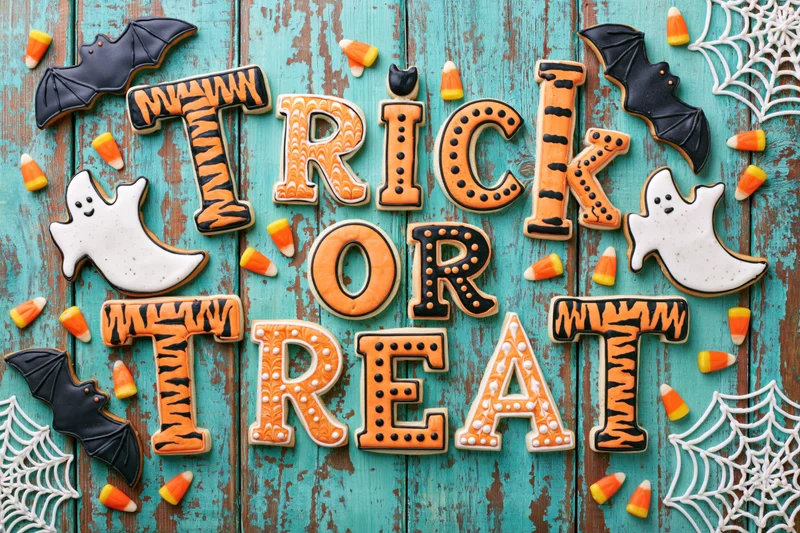Halloween sugar cookies spelling trick or treat on a teal wooden surface with candy corn and decorations