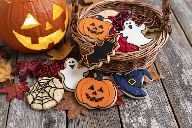 Halloween decorated sugar cookies arranged with jack-o-lantern and autumn leaves on rustic wood table