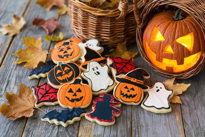 Halloween decorated sugar cookies arranged on rustic wooden table with jack o lantern and autumn leaves
