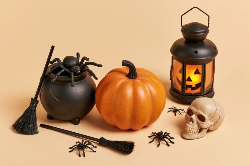 Halloween decorations including pumpkin, lantern, skull, spiders, broom and cauldron arranged on a warm cream surface