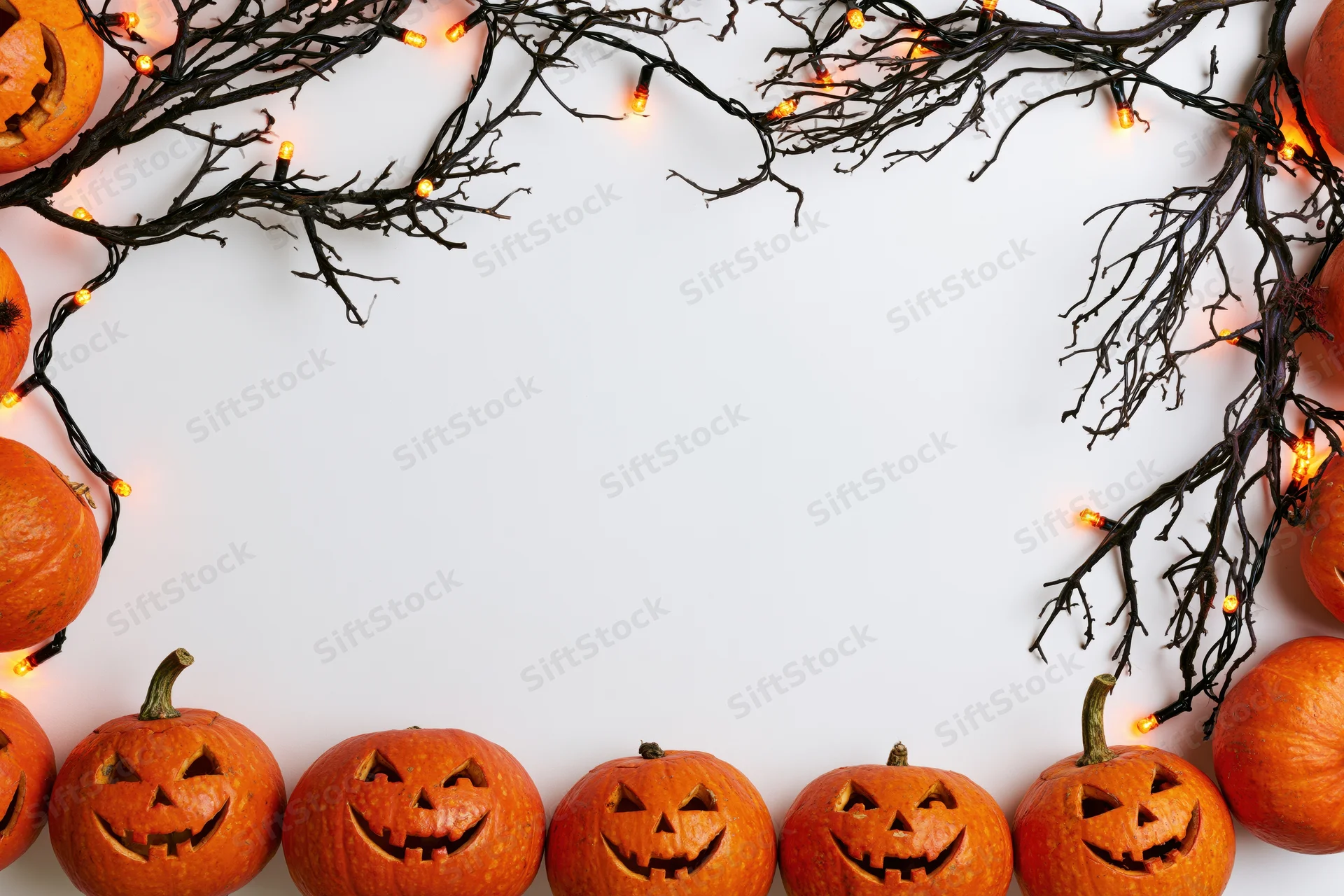 Carved pumpkins and glowing lights arranged along white surface edges for halloween flat lay