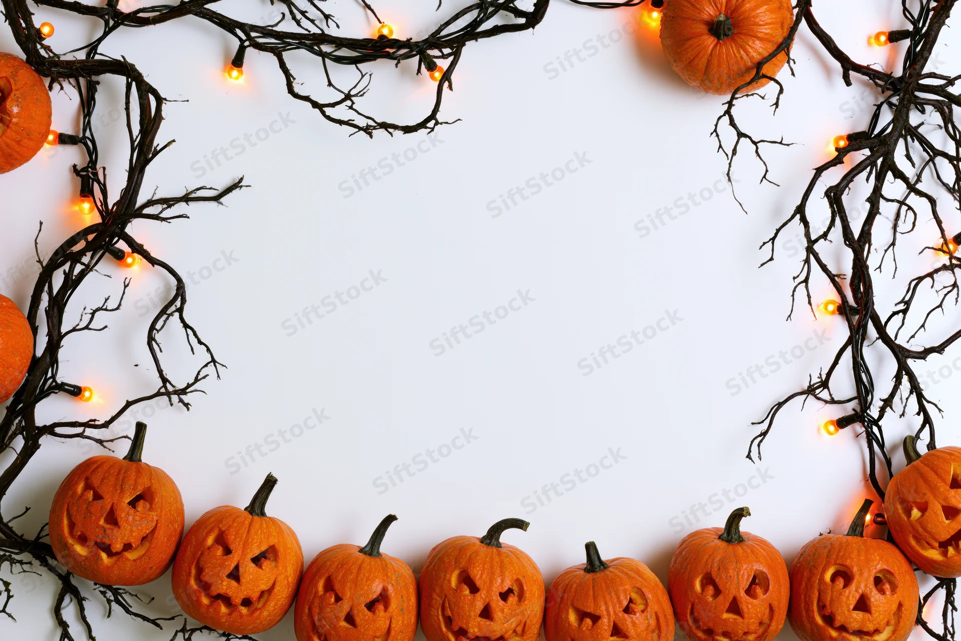 Carved jack-o-lanterns and twigs with string lights arranged in a frame on white background