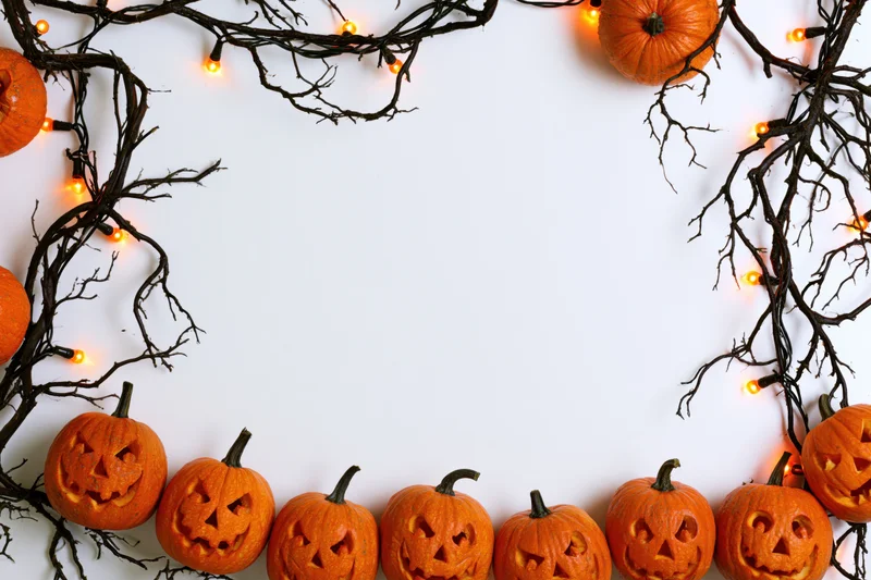 Carved jack-o-lanterns and twigs with string lights arranged in a frame on white background