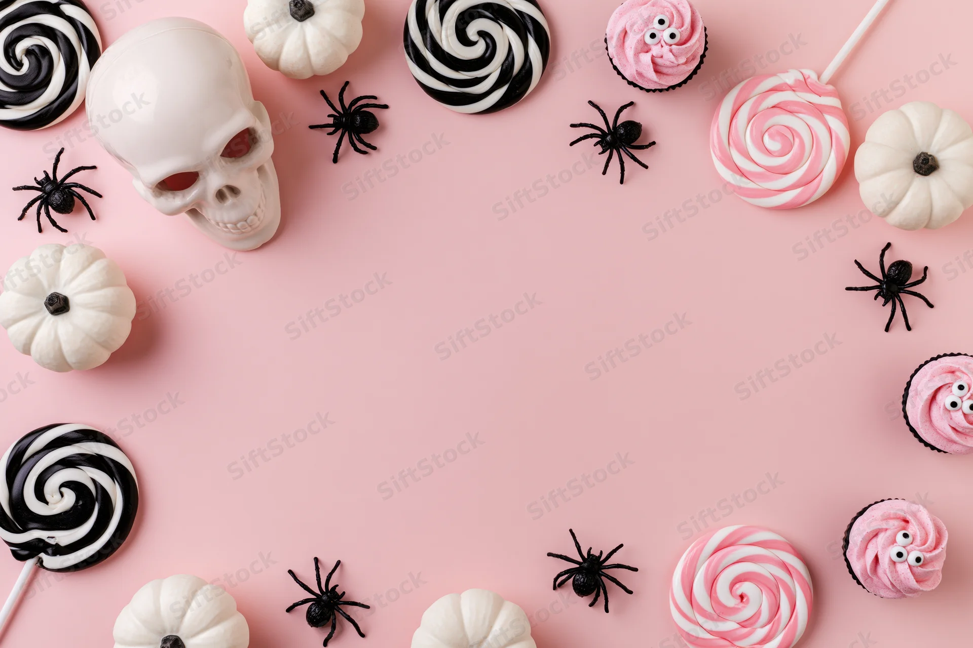 Halloween flat lay with candy, skull, pumpkins and spiders arranged around pink background with copyspace