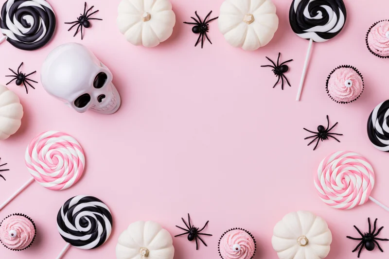 Halloween flat lay with candy, pumpkins, skulls and spiders arranged around pink background with copyspace